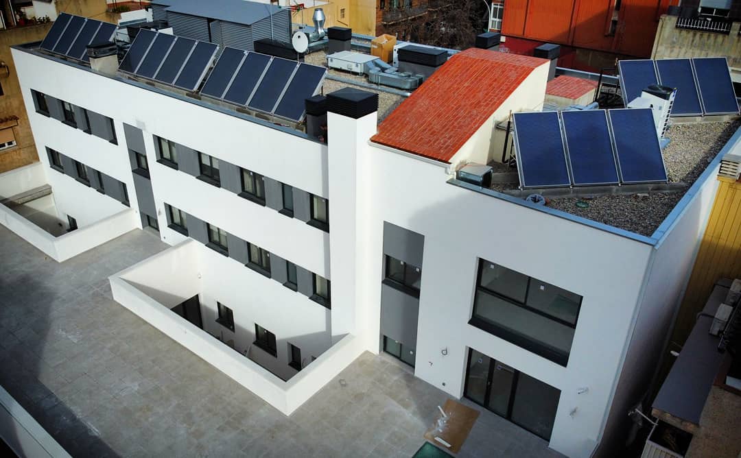 Vista aérea de un moderno edificio blanco con múltiples ventanas de aluminio oscuro y paneles solares instalados en la azotea en Badalona.