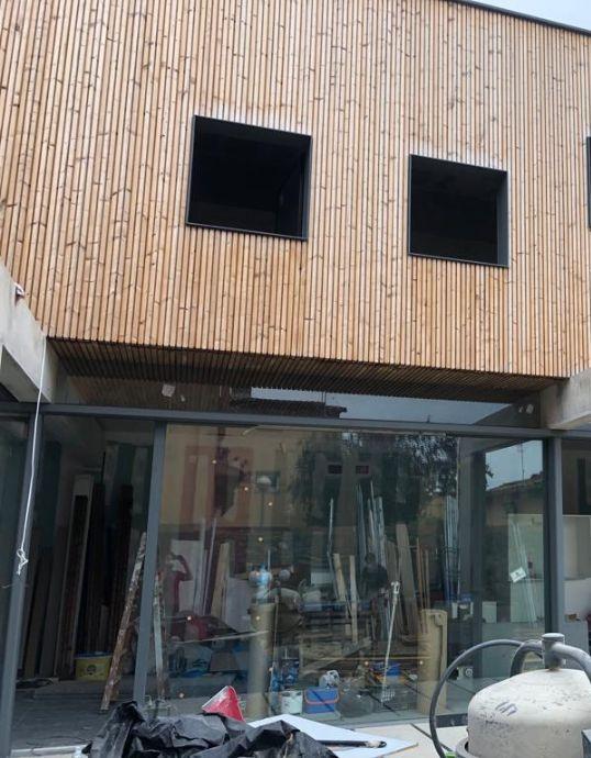 Grandes vidrieras de aluminio en planta baja bajo una fachada voladiza de lamas de madera con ventanas oscuras.