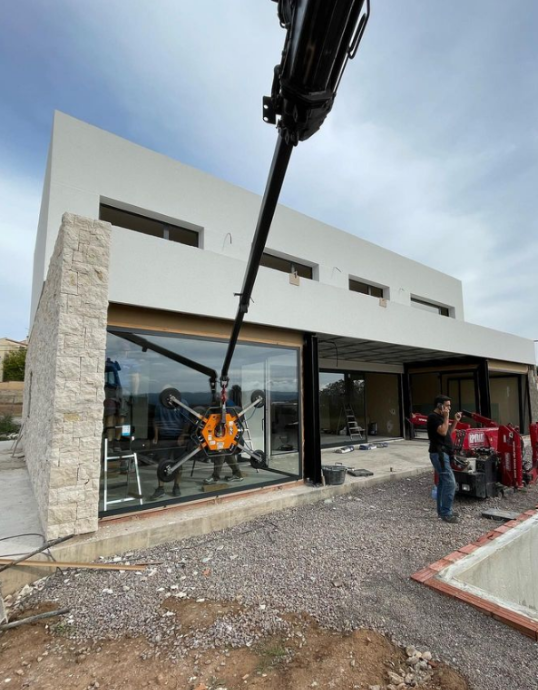 Operario utilizando una grúa con sistema de ventosas para instalar un cristal pesado de gran tamaño en la planta baja de una casa.