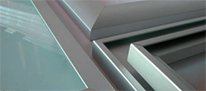 Detalle en primer plano de junquillos y perfiles complementarios de aluminio en acabado gris metalizado, mostrando el ensamblaje de precisión geométrica con el panel de vidrio.