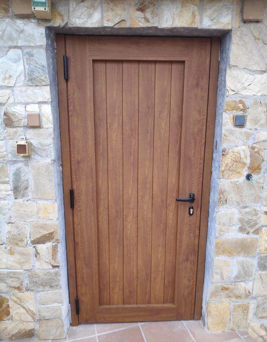 Puerta peatonal exterior de aluminio con diseño de lamas verticales acabado madera en Casa en Vilassar de Dalt.