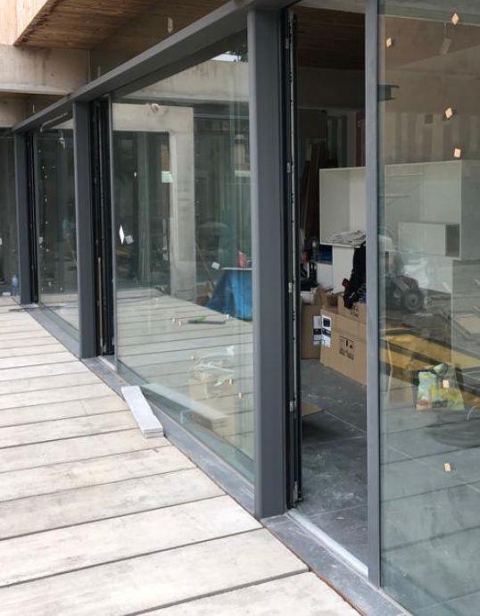 Grandes puertas correderas de cristal con marcos de aluminio oscuro abiertas hacia una terraza de madera en la Casa en el Vallès.