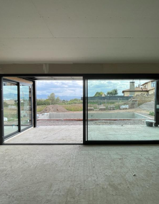 Vista interior de un salón en obras con grandes puertas correderas de aluminio abiertas hacia la zona del porche y la piscina.