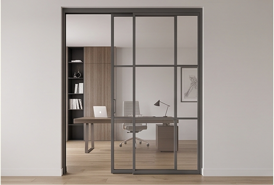 Moderna oficina interior separada por una elegante puerta corredera de aluminio gris de la Serie CR89 Apotema, dividida en cuadrículas acristaladas.