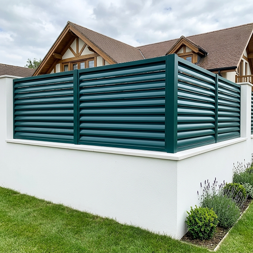 Valla perimetral de una vivienda formada por un muro blanco y un sistema de celosía fija con lamas horizontales de aluminio lacado en verde oscuro.